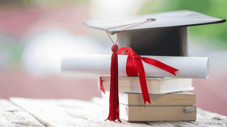 Image of a graduation cap with graduation certificate and books piled together.