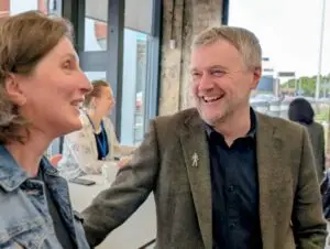 David smiles talking to Hilary in a conference setting