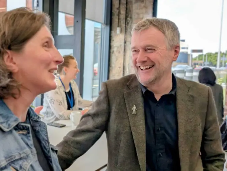 David smiles talking to Hilary in a conference setting