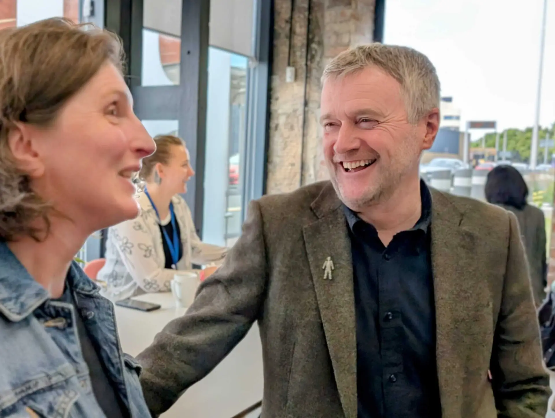 David smiles talking to Hilary in a conference setting
