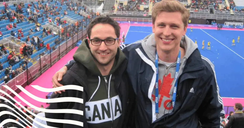 Two men beside each other with hockey pitch below.