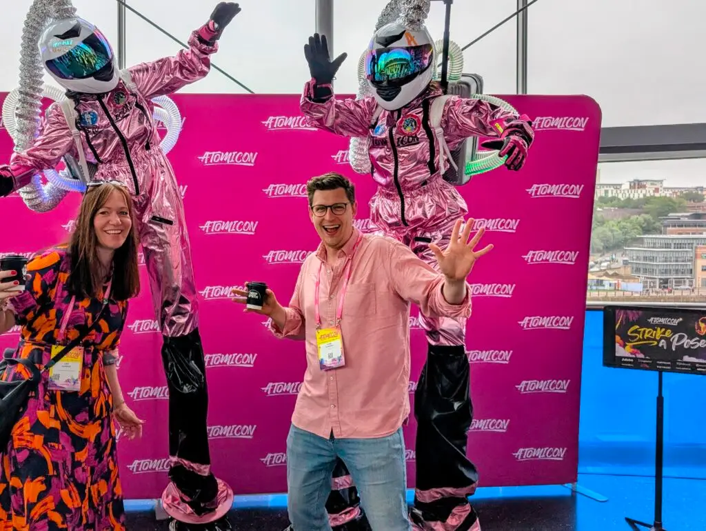 Smiling people with robot performers in the background at Atomicon