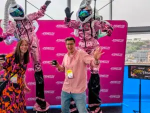 Smiling people with robot performers in the background at Atomicon