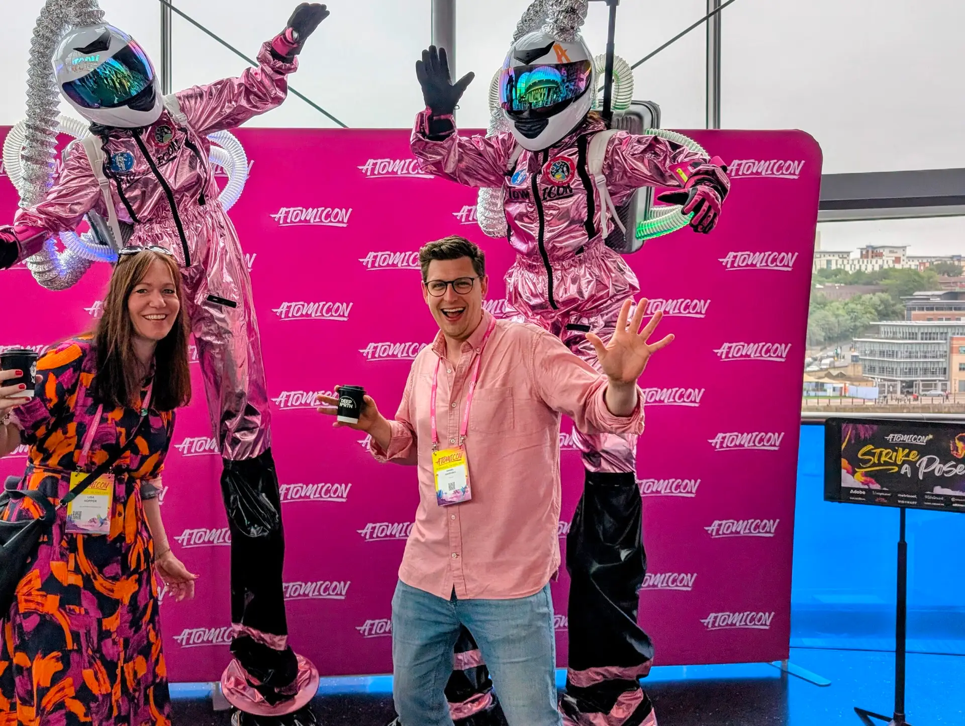 Smiling people with robot performers in the background at Atomicon